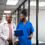 male nurse talks to doctor in corridor holding clipboard